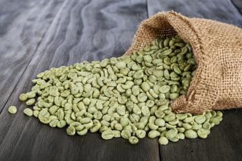 burlap sack of green coffee beans on old wooden table