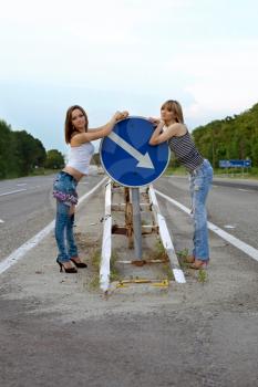 Royalty Free Photo of Two Women in the Centre of the Road With an Arrow Sign