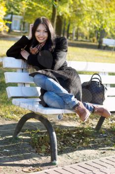 Smiling young woman sitting on a bench in autumn park