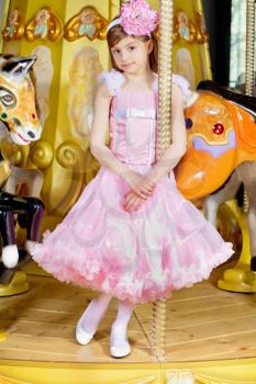 Pretty little girl in pink lace dress standing on the carousel
