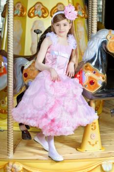 Elegant little girl in beautiful pink dress posing on the carousel