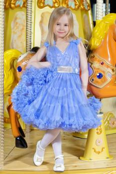 Adorable little girl in blue dress posing near the carousel pony