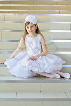Little girl in white dress, shoes and tights posing on the steps