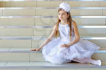 Little thoughtful girl in white dress sitting on the steps