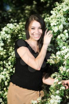 Pretty smiling brunette posing near the flowering bush