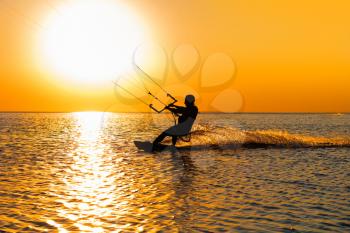 Silhouette of a kitesurfer sailing at sunset