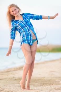 Young cheerful blond woman in blue blouse posing on the beach