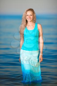 Pretty smiling blonde wearing blue t-shirt and skirt posing in water
