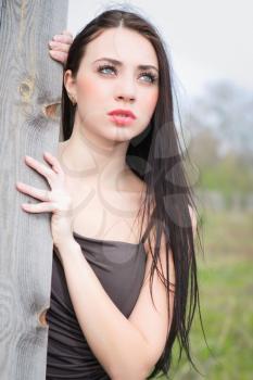 Portrait of thoughtful young brunette posing at the wooden fence