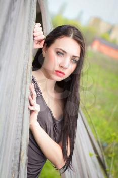 Pretty young thoughtful brunette posing behind the wooden fence