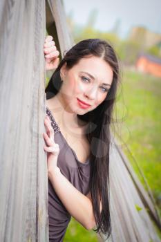 Smiling young brunette in gray dress posing behind the wooden fence