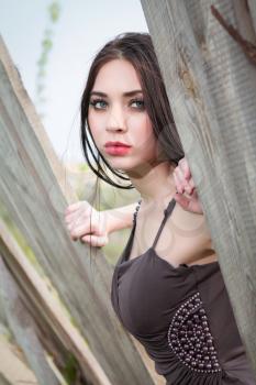 Young thoughtful brunette in dress posing behind the wooden fence