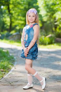 Nice little blond girl in blue jeans dress posing outdoors