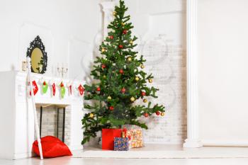 Decorated fir tree and gift boxes near fireplace in living room