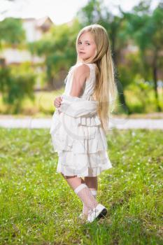 Little blond girl wearing white dress posing outdoors