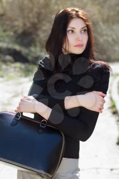 Thoughtful brunette in black blouse with big bag posing outdoors