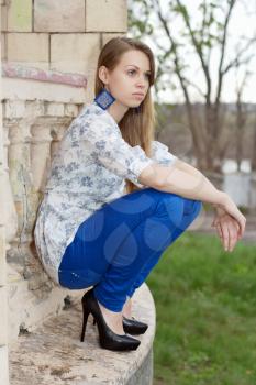Young thoughtful blond woman sitting on the building facade