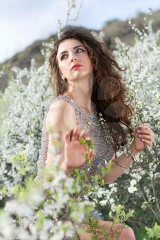 Beautiful curly caucasian lady wearing grey dress posing in blooming garden