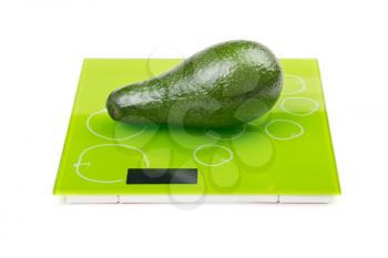 Green avocado on square kitchen scales. Isolated