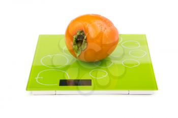 Persimmon fruit on square kitchen scales. Isolated