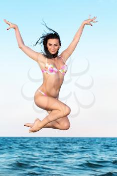 Pretty brunette in swimsuit jumping above the sea