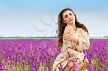 Pretty thoughtful brunette sitting in a flowering field