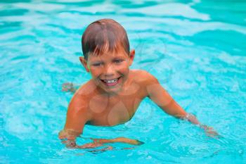 Smiling boy swims in pool on summer vacations