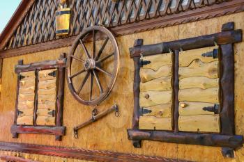 Old style wooden cottage with decorative wheel between shuttered windows