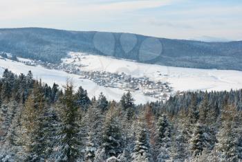 Royalty Free Photo of a Snowy Village in a Valley Between Forested Mountains