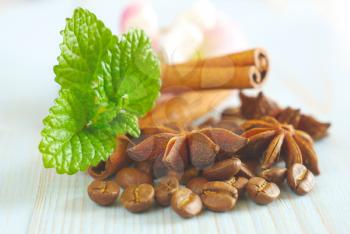 Coffee grains with anise star, fresh green mint leaves and cinnamon sticks on vintage wooden table food ingredients background