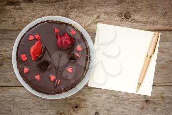 Chocolate cake with note paper and pen on the wooden background