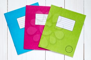 Three colored exercise books on the white wooden background