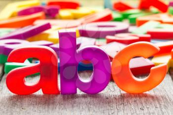 ABC spelling and pile of colorful plastic letters on wooden background