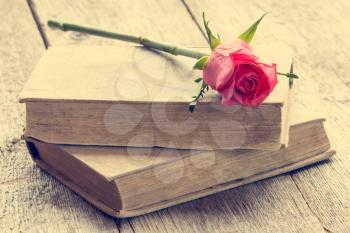 Two old books with rose, lying on the old floor. Vintage filter.