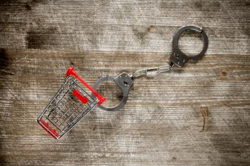  Shopping cart and handcuffs on old wooden background.Top view.