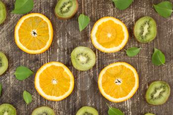 Sliced kiwi and orange fruits with green leaves on wooden background