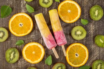   Popsicles with sliced orange and kiwi fruit on wooden background. Top-view.
