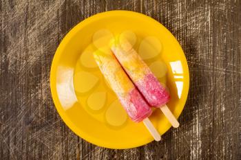 Two  Raspberry and Orange ice pops on a yellow plate