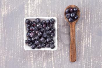   Wooden spoon and white bowl with fresh blueberries on grey wooden background