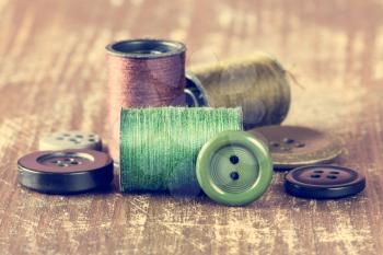 Spools of thread and buttons on wooden background. Image has been filtered to give a retro or vintage style.
