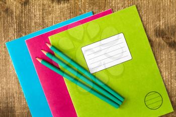  Three colored exercise books and three pencils on the wooden background