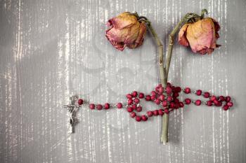 Catholic rosary and faded roses on grey wooden background