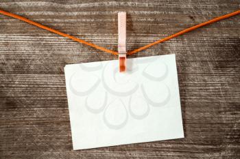 Blank paper sheet hanging on a rope over wooden background