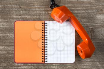 Orange telephone receiver and blank notebook for copy-space