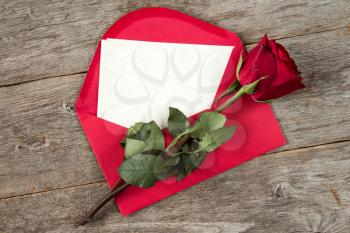 Red envelope with blank letter and faded rose on wooden background