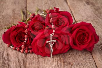 Silver crucifix and bunch of red roses on wooden background