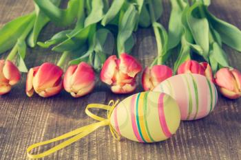 Two Easter eggs and blooming tulips on wooden background