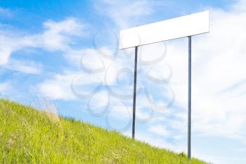 Blank sign board on a background of green grass and blue sky