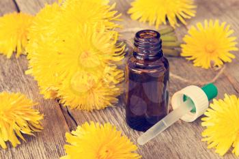Dandelion flowers and small bottle with dropper on wooden background