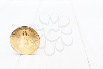 One golden bitcoin on white wooden background